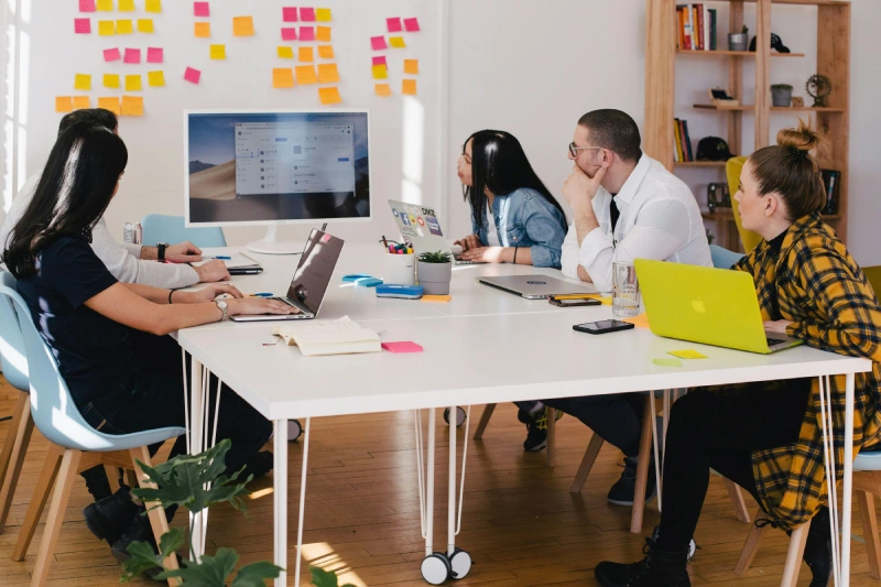 Design team collaborating around a desk while reviewing website layouts on a computer